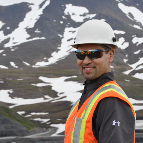 Man in safety gear smiles against a snowy mountain backdrop.